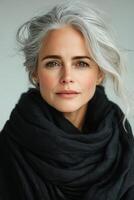 A woman with elegant gray hair wearing a black scarf poses against a neutral background photo