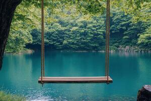 A wooden swing hanging by the calm blue lake surrounded by lush green trees during daytime photo