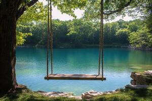 A wooden swing hanging by the calm blue lake surrounded by lush green trees during daytime photo