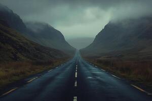 Dark and moody landscape with a winding road leading to distant mountains on a rainy day photo