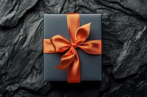 Elegant black gift box with orange ribbon on a dark background suitable for various celebrations photo