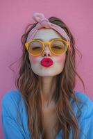 Young woman poses playfully with pink headband and retro sunglasses against a pastel backdrop photo