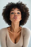A woman with curly hair poses playfully in a neutral toned sweater against a light background photo