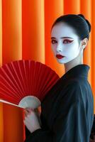 Young woman in traditional attire posing with a fan against a vibrant orange background photo