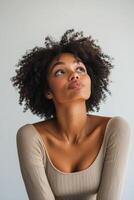 A woman with curly hair poses playfully in a neutral toned sweater against a light background photo