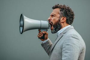 Man wearing a suit passionately speaks into a megaphone against a gray background outdoors photo