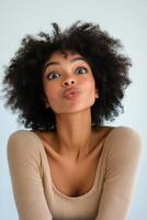 A woman with curly hair poses playfully in a neutral toned sweater against a light background photo