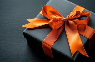 Elegant black gift box adorned with a bright orange ribbon on a dark textured surface photo