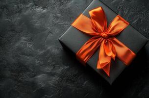 Elegant black gift box with orange ribbon on textured dark surface photo