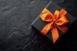 Elegant black gift box adorned with a bright orange ribbon on a dark textured surface photo