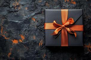Elegant black gift box adorned with a bright orange ribbon on a dark textured surface photo