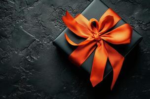Elegant black gift box adorned with a bright orange ribbon on a dark textured surface photo