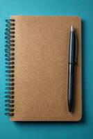 A brown notebook and a black pen resting on a teal table surface during daytime photo
