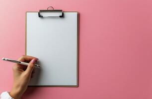 Taking notes on a clipboard with a blank page and a pen on a pink background photo