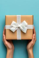 A person holding a beautifully wrapped gift with a white ribbon against a bright blue background photo
