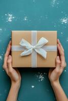 A person holding a beautifully wrapped gift with a white ribbon against a bright blue background photo