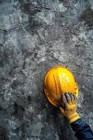 Construction worker placing yellow hard hat on textured gray wall in building site area photo