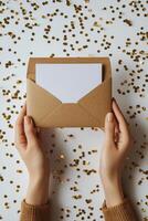 Hands holding a brown envelope with a blank card surrounded by golden confetti photo