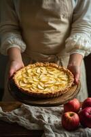 A baker presents a freshly made apple pie on a wooden pedestal surrounded by fresh apples photo