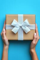 A person holding a beautifully wrapped gift with a white ribbon against a bright blue background photo