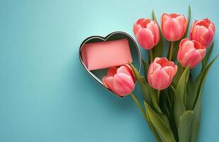 Pink tulips arranged beside a heart shaped box on a light blue background photo