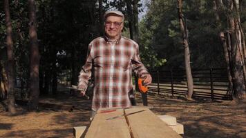 An elderly craftsman demonstrates the tools he uses in his work while building a wooden house. video