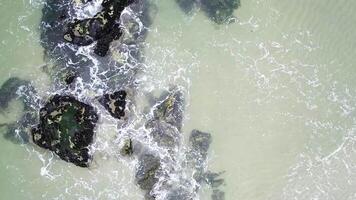 rocks on the shore of a beach with the waves of a calm sea, aerial view from the top with drone. Beach background concept video