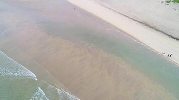shore of a beach at sunrise with calm sea and two people walking with a dog, aerial view with drone footage video