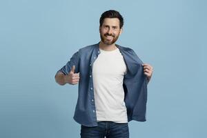 Handsome man smiling showing thumbs up and opening shirt on blue background photo