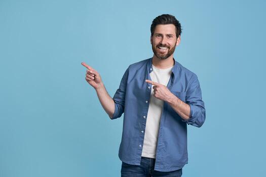 Happy man pointing two index fingers to empty space on blue background photo