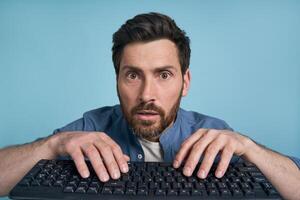 Shocked man typing on keyboard with blue background photo