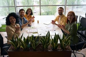 Happy business people clapping hands sitting at office desk photo