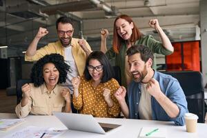 Excited business team celebrating success looking at laptop in office photo