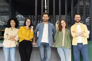 Five young professionals smiling while leaning on a counter in a modern office photo