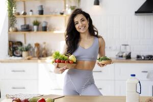 Young woman holding bowls with vegetables and microgreens in kitchen photo
