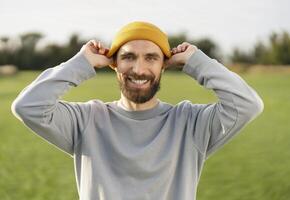 Portrait of a smiling man adjusting his yellow beanie in a field photo