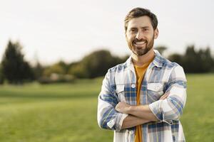 Portrait of a smiling farmer standing in green field with crossed arms photo