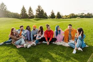 Group of diverse young people relaxing and socializing together on a blanket in a park photo