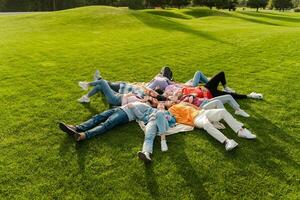 Group of friends relaxing lying down in circle on grass in park photo