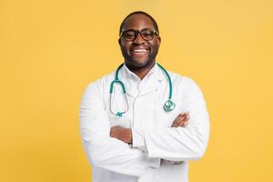 Happy African American man wearing doctor uniform with crossed arms isolated on yellow photo