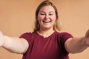 Smiling Caucasian plus size woman making selfie looking at camera isolated on beige photo