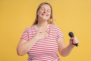 Smiling plus size woman enjoying singing holding hand on chest in studio photo