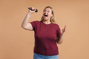 Plus size woman singing loudly into a mic posing in studio photo
