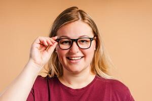Portrait of positive plus size woman in glasses posing isolated on beige background photo