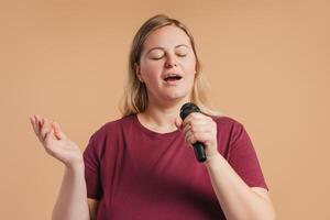 Calm plus size woman closing eyes singing using microphone in studio photo