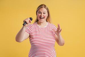 Happy plus size woman enjoying singing holding microphone looking at camera photo