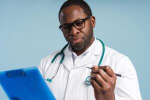 African American doctor making notes posing in studio, isolated on blue photo