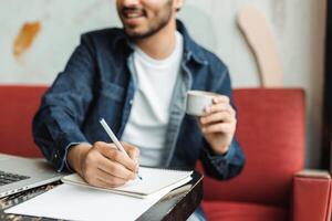 Young man writing on notepad and drinking coffee in cafe photo