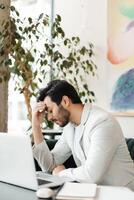 Stressed businessman having headache while working on laptop in cafe photo