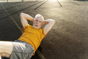 Senior man doing sit ups on a running track in the golden hour sunlight photo